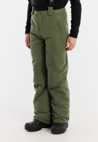 Groene sneeuwbroek met een gevoerde textuur, cargopockets, verstelbare schouderbanden en een aansluitende taille voor warmte en mobiliteit. Zwarte laarzen zichtbaar.