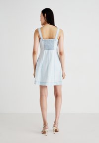 Light blue denim dress with smocked back, square neckline, and adjustable straps. Features a flared hem and subtle distressing details.