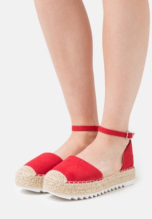 Red suede espadrille wedges with a woven jute sole, ankle strap, and white rubberized outsole. Features rounded toe and stitched detailing.