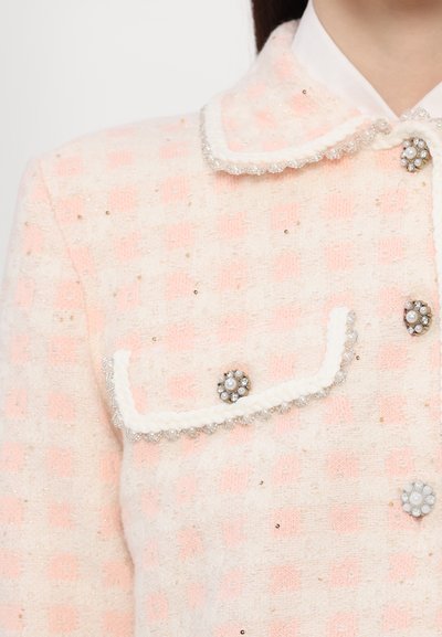 Tweedjacke in Creme und sanftem Rosa, mit Kragen, dekorativen Knöpfen mit Perlen und einem strukturierten Muster mit goldenen Akzenten.
