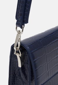 Granatowa torebka z ekoskóry o fakturze imitującej krokodyla, z połyskującą powierzchnią, wyposażona w srebrną metalową klamrę i o konstrukcji o prostokątnym kształcie.