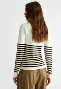 Maglione a maglia a righe in crema, nero e oro. Caratterizzato da maniche lunghe e texture a coste sulle spalle. Design aderente con polsini in contrasto.