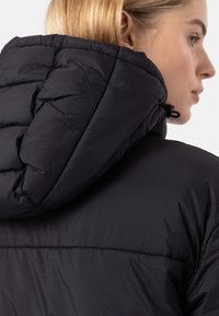 Black puffer jacket with a textured surface, featuring a large, quilted hood and adjustable drawstring, seen from the side and back.