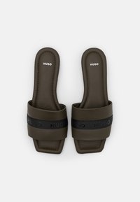 Une paire de sandales à glisser de couleur marron foncé avec des détails de sangle noire embossés avec 'HUGO' sur un fond blanc.