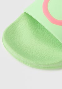Green rubber slide sandal with a textured footbed and a smooth upper. Features a circular pink accent on the strap.