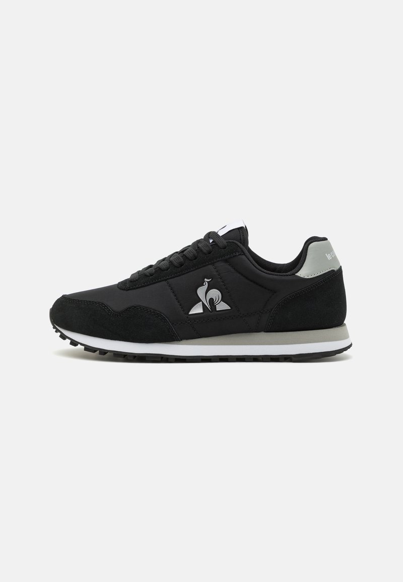 Black sneakers featuring a combination of smooth and textured materials, prominent logo, and a contrasting white midsole with a black outsole.