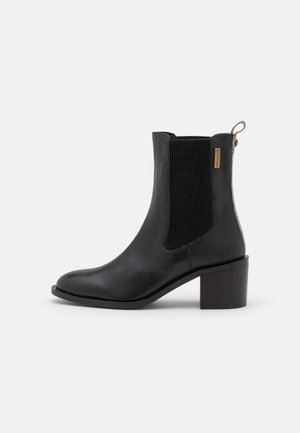 Bottines en cuir noir avec un panneau latéral en élastique côtelé et une petite languette. Elles présentent un talon épais et une finition lisse.