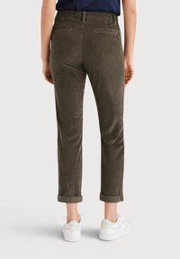 Olivgrön kordfløyelsbyxor med smal benvidd, med uppvikta fållar, två bakfickor och en slät yta. Kombinationen är med vita sneakers.