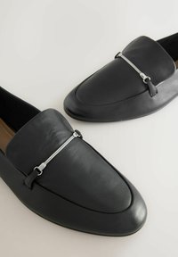 Čierne kožené mokasíny s elegantným dizajnom, s akcentom striebornej farby cez hornú časť, špicatou špičkou a hladkou textúrou.