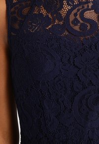 Navy blue lace fabric featuring floral and paisley patterns, with a textured, layered design. Close-up view showcasing details and intricacies.