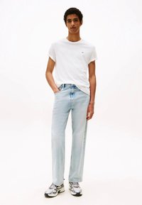 Hele sinised sirge lõikega teksapüksid kõrge vöökohaga, kombineeritud valge lühikese varrukaga T-särgiga. Modell kannab hõbedasi tossusid.