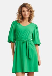 Groene jurk met korte mouwen en een V-hals, vastgezet met een riem op de taille, gemaakt van een glad materiaal met een losse pasvorm en gathered pofdetails op de mouwen.