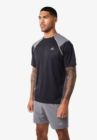 Czarny sportowy T-shirt z szarymi akcentami na ramionach, krótkie rękawy i logo. W połączeniu z jasnoszarymi szortami o prostym wzorze.