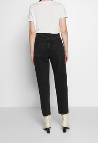 Jeans neri a vita alta con design a gamba dritta, denim testurizzato, dotati di due tasche posteriori. Abbinati a una t-shirt bianca a maniche corte.