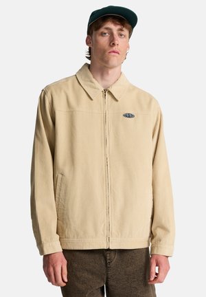 Giacca in velluto a coste color beige con scollo a collo, cerniera frontale, tasche laterali e logo discreto sul petto. Tessuto strutturato con motivo a coste.