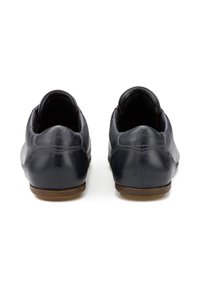 Scarpe in pelle blu scuro con una texture liscia, punta arrotondata, profilo basso e suole in gomma marrone. Dettaglio di cuciture lungo la parte posteriore.