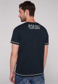 Camiseta de manga corta azul marino de algodón, con un estampado gráfico en la parte posterior, costuras blancas en las mangas y un corte relajado.