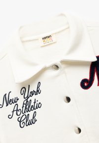Biała koszulka polo dla dzieci z haftem "New York Athletic Club" w granatowym kolorze oraz trzema metalowymi zatrzaskami z przodu.