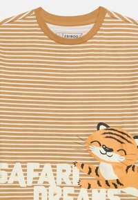 Ριγέ καφέ και λευκό πουκάμισο με το κείμενο "Safari Dreams" και ένα χαμογελαστό καρτούν τίγρη στο κάτω δεξιό μέρος.