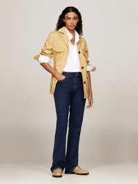 Beige arbetsjacka med uppkavlade ärmar, vit skjorta med krage, mörk denim med utsvängda jeans och beiga skor med svarta accenter.