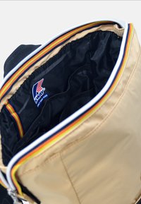 Beżowa torba z czarnym wnętrzem, z wielokolorową, paskowaną podszewką i białym zamkiem. Wewnątrz widoczne logo K-Way.