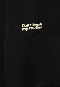 Zwarte sweatshirstof met een zachte textuur. Heeft een voorzak en bedrukt tekst "Don't break my routine" in crèmekleur.