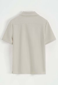 Polo shirt beige à manches courtes en tissu texturé, avec un col classique, un ourlet droit et des fentes sur les côtés pour plus de liberté de mouvement.