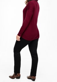 Bordowy sweter o luźnym kroju z długimi rękawami, zestawiony z czarnymi spodniami o dopasowanym kroju i brązowymi, wzorzystymi botkami za kostkę.