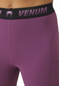 Violetinės legging trousers su prigludusia dizainu, pagamintos iš elastingos medžiagos. Savybė - juodos elastingos juostos su rožiniu "VENUM" logotipu ir šonine kišenė.