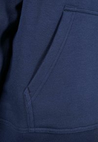 Sudadera de color azul marino con textura y un bolsillo tipo canguro. Cuenta con un acabado de tela suave y puños ribeteados en las mangas y en el dobladillo para mayor estructura.