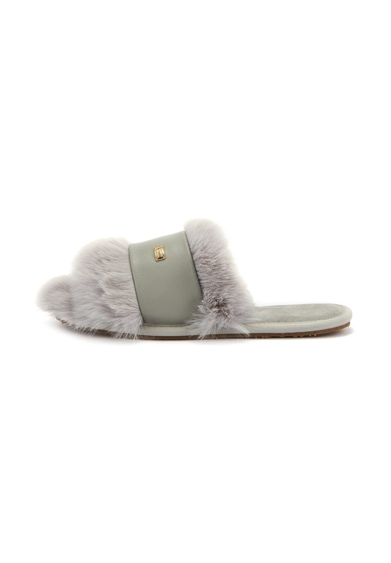 Chaussons en fausse fourrure grise avec une bande en cuir verte, semelle plate et détail en emblème doré. Texture douce avec des accents duveteux.