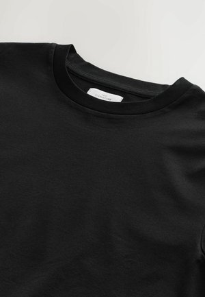 Schwarzes Baumwoll-T-Shirt mit Rundhalsausschnitt, das eine glatte Textur und kurze Ärmel aufweist. Das Etikett am Ausschnitt trägt die Aufschrift "NXT SIGNATURE."