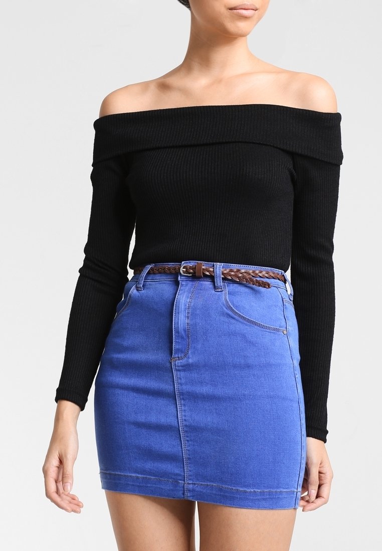 Femme portant un haut noir à manches longues épaules dénudées et une mini-jupe en jean bleu avec une ceinture tressée marron.
