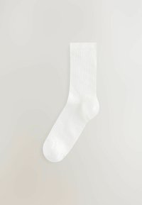 Vit bomullsstrumpa med ribbad textur, rund tå och flexibel mudd. Designad för komfort och enkel stil.