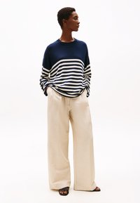 Suéter de rayas en azul marino y blanco de corte oversize, combinado con pantalones de pierna ancha en crema y sandalias negras. Texturas suaves y silueta relajada.