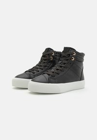 Baskets montantes noires en matériau synthétique lisse, avec des œillets en bronze, des lacets noirs texturés et une semelle en caoutchouc blanc.