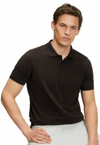Czarna koszulka polo z krótkimi rękawami i zapięciem na trzy guziki. Gładka faktura, dopasowany fason, noszona z szarymi spodniami dresowymi.
