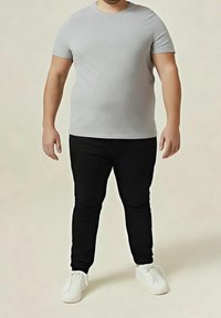 Harmaa lyhythihainen T-paita, mustat slim-fit-housut ja valkoiset slip-on-kengät. Yksinkertainen, rento muotoilu ja sileä pinta.