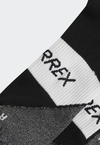 Calcetines deportivos en blanco y negro con tejido texturizado, que presentan un patrón geométrico y una marca visible "Terrex" en negro en contraste.