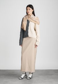 Kötött pulóver, amely krém és sötétszürke részekből áll, egy bézs hosszú szoknyával párosítva. Egy világosbarna sál lóg a vállon. Fekete pántos magassarkú cipő.