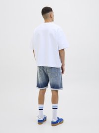 White oversized t-shirt, denim shorts with rolled cuffs, blue sneakers, and white socks with blue stripes. Back view.