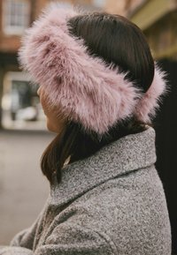 Bandă de urechi din blană sintetică în roz deschis, cu o textură pufoasă. Purtați-o peste părul închis la culoare, asortată cu o haină texturată gri.