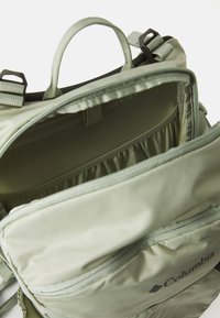 Zaino verde chiaro con molteplici scomparti, anelli in tessuto e cerniere. L'interno presenta tasche elastiche e una fodera liscia.