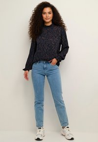 Tmavomodrá blúzka s dlhým rukávom so vzorom paisley, zaobleným výstrihom a pohodlným strihom. Kombinovaná s svetlomodrými úzkymi džínsami a bielymi teniskami.