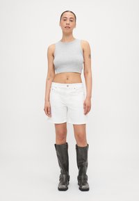 Top corto gris, pantalones cortos blancos y botas grises hasta la rodilla con hebillas. La modelo está de pie frente a un fondo blanco sencillo.