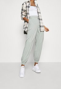 Jasnozielone spodnie cargo z elastycznymi mankietami, bocznymi kieszeniami i luźnym krojem, połączone z białym topem na ramiączkach oraz koszulą w kratę z guzikami.