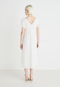 Valge midi kleit hõljuvate varrukatega, V-tagusega, elastse vöökohaga ja pitsist ääristusega. Kantud hõbedaste rihmadega kõrgete kontsadega, näidates lihtsat, aga samas elegantset disaini.