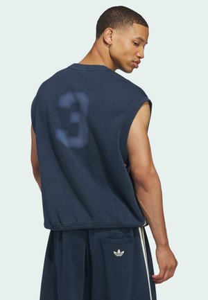 Mand iført navy ærmeløs skjorte med udvasket nummer 3 på ryggen og matchende Adidas shorts med logo på lommen, ser over sin skulder.
