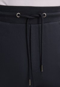 Marinefarbene Jogginghosen mit einem Kordelzug-Bund, ausgestattet mit silberfarbenen Ösen und Enden, gefertigt aus einem weichen, strukturierten Material.