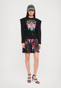 Zwarte sweatshirt met levendige bloemembroidery, zwarte rok met kleurrijk bloempatroon en zwarte sandaaltjes met bandjes; casual pet.